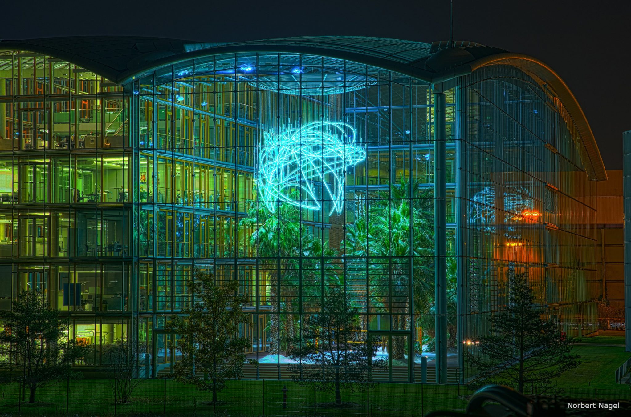 GBMpic_ Moderner Glasbau bei Nacht mit großer Neonlichtinstallation und sichtbarer Innenbegrünung.